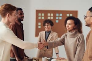 two people shaking hands on a business deal with others around